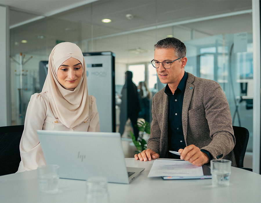 Zwei Mitarbeitende im Personalbereich besprechen Bewerbungsunterlagen am Laptop im Büro